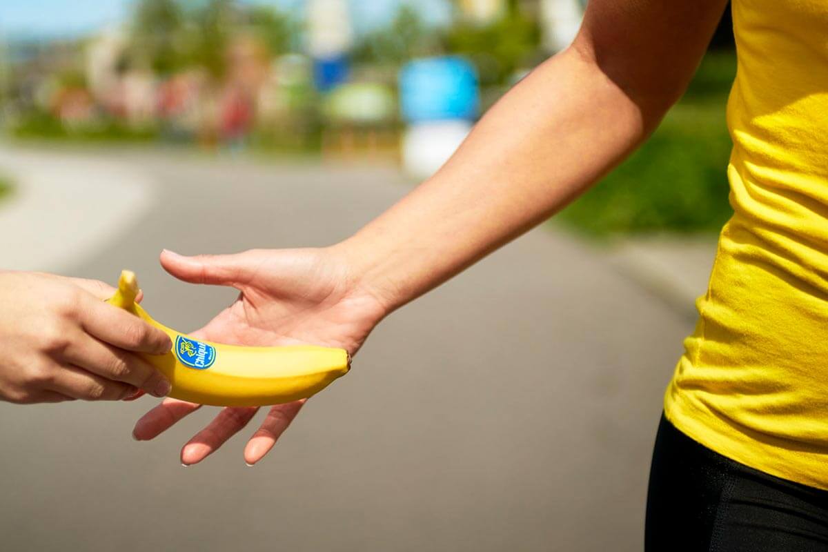 Banan z masłem orzechowym na energię Pokrojony banan polany gęstym masłem orzechowym obok garści migdałów na desce