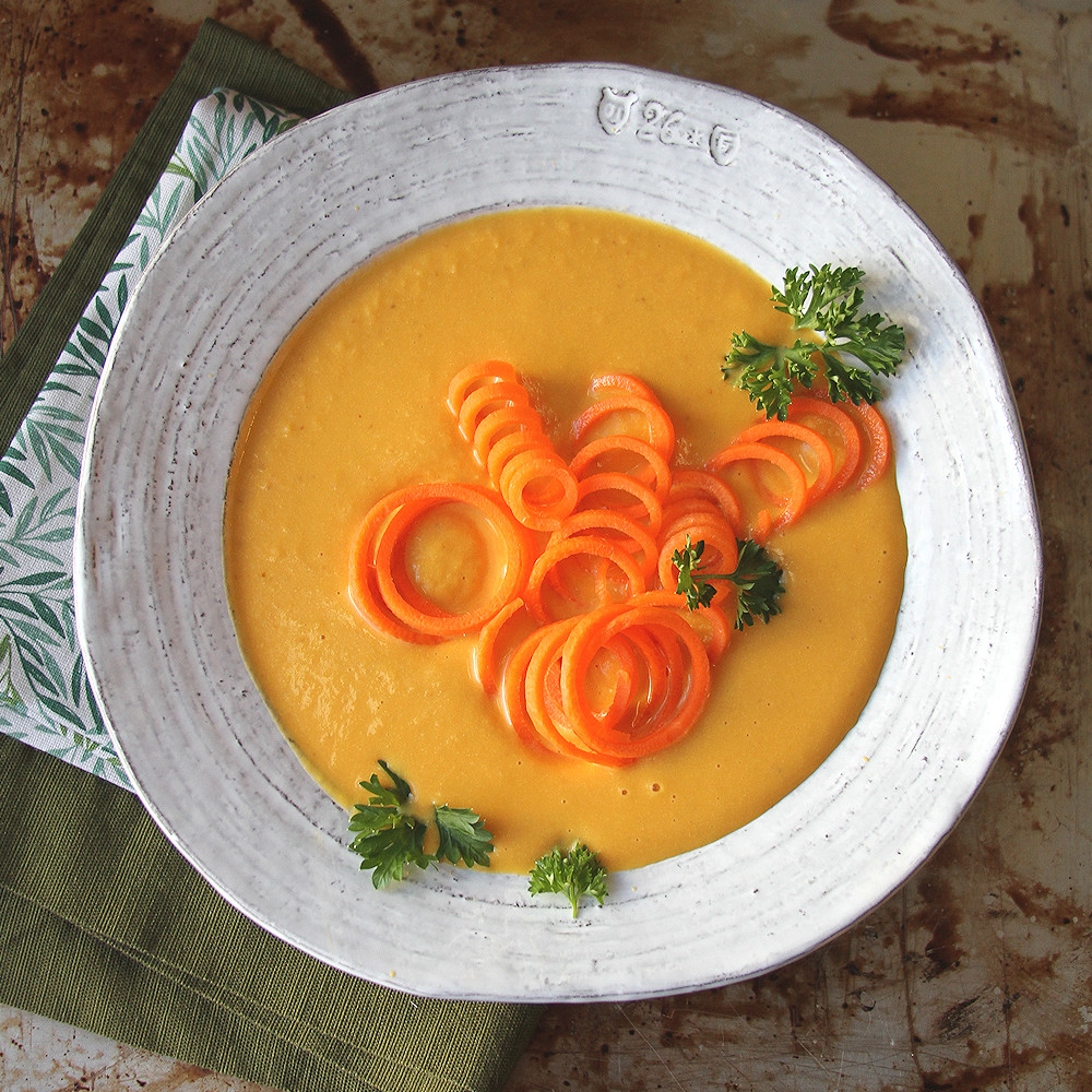 Zupa krem marchewkowa z dodatkiem śmietany Kremowa zupa marchewkowa w miseczce z kleksem śmietany i ziołami na wierzchu