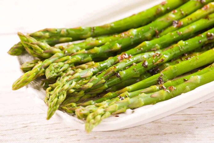 zielone szparagi ugotowane na parze polane roztopionym masłem na białym talerzu